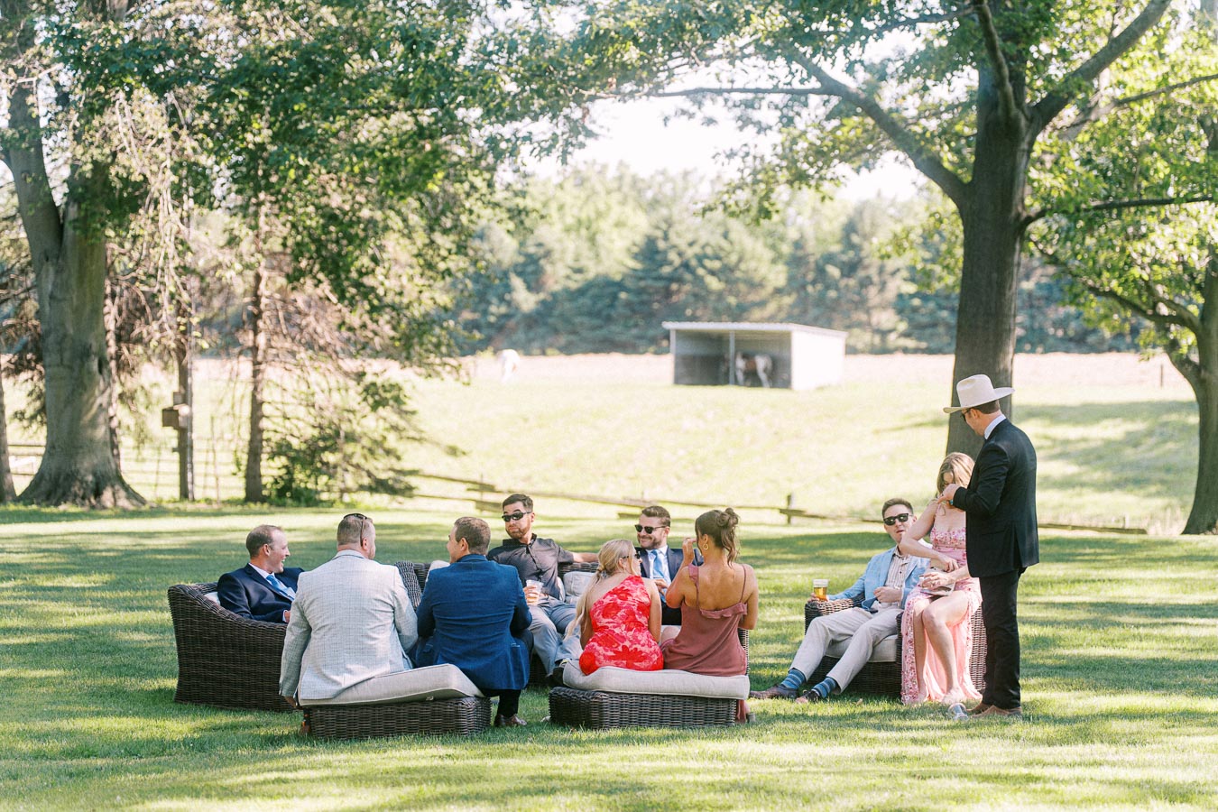 Wedding guests relaxing on outdoor lounge furniture under trees at a private farm estate near Chatham-Kent, Ontario, Canada.