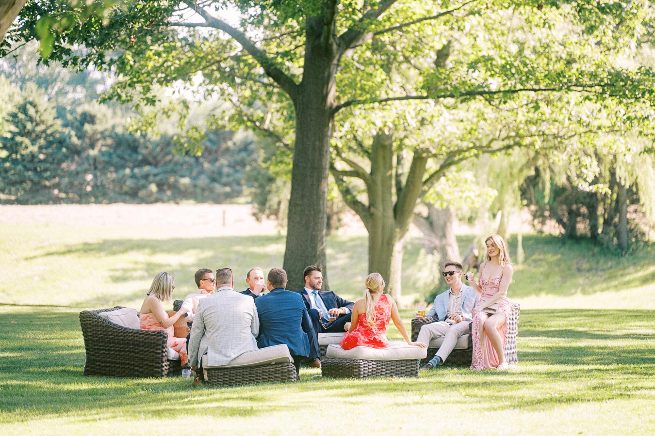 Wedding guests relaxing on outdoor lounge furniture under trees on a private farm estate near Chatham-Kent, Ontario, Canada.