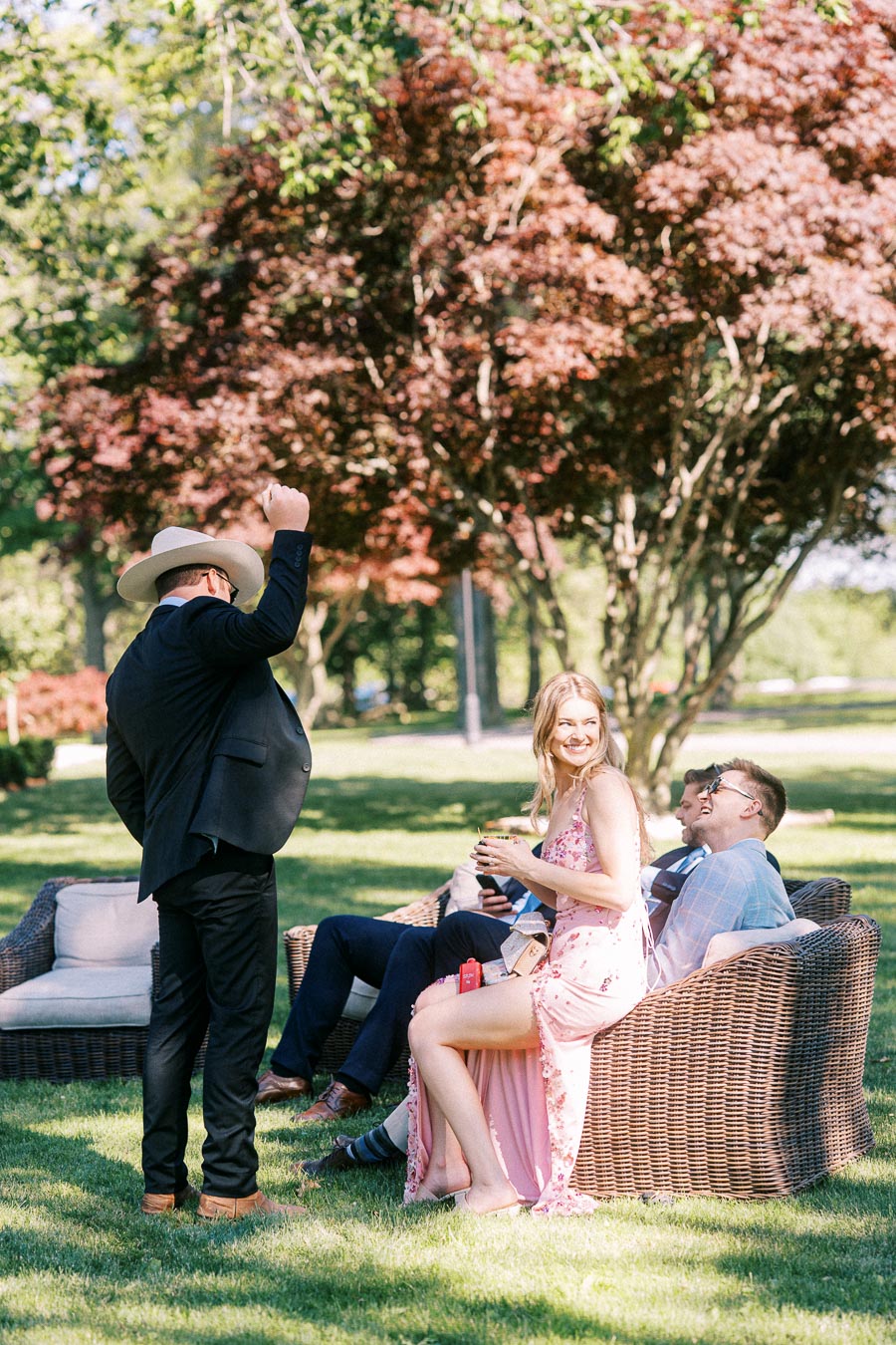 Guests relax on wicker outdoor seating during a private estate wedding near Chatham-Kent, Ontario, Canada, with trees and lawn in the background.