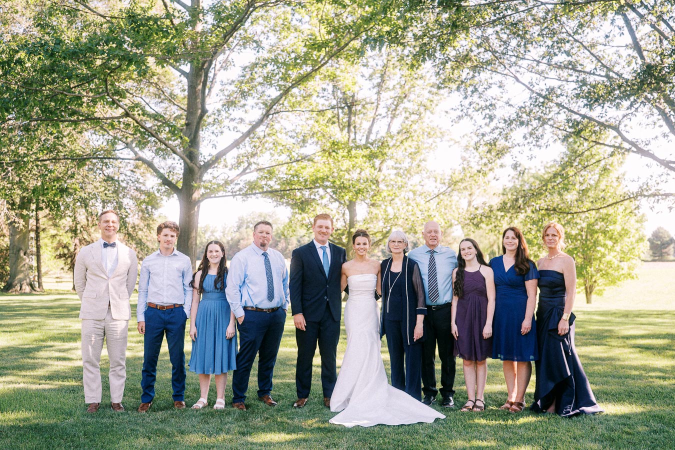 Wedding family portrait outdoors on a private farm estate near Chatham-Kent, Ontario, with bride, groom, and guests standing under trees.
