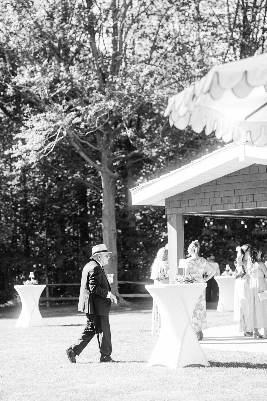 Black and white outdoor wedding cocktail reception on a private estate near Chatham-Kent, Ontario, with guests, cocktail tables, trees, and a tented pavilion.