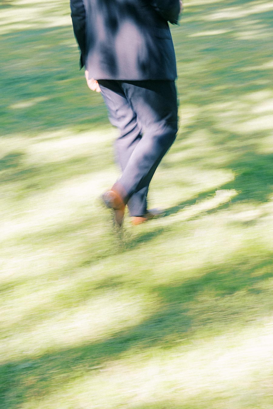Motion blurred groom in a dark suit walking across sunlit green grass at an outdoor private estate wedding in Ontario.