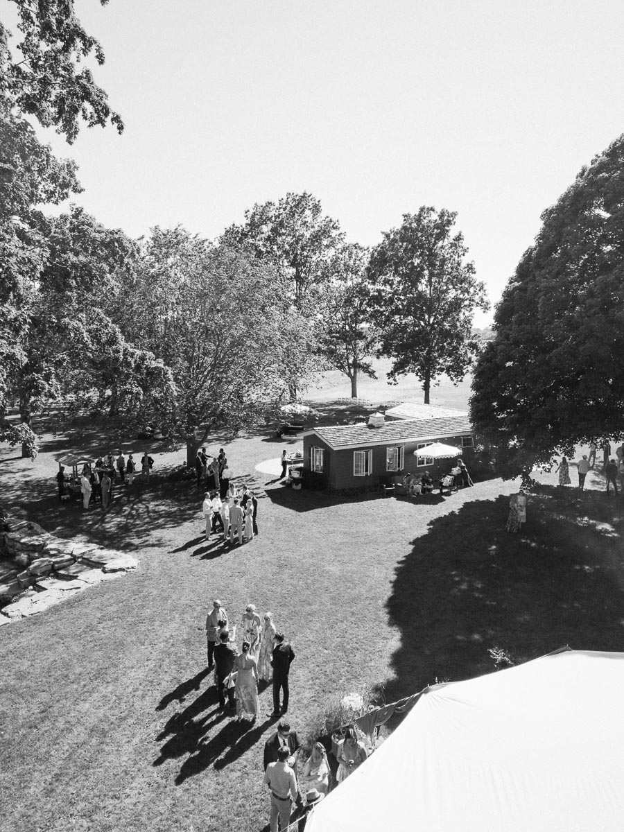 Black and white view of an outdoor farm wedding on a private estate near Chatham-Kent, Ontario, with guests gathered on a lawn beside a tent.