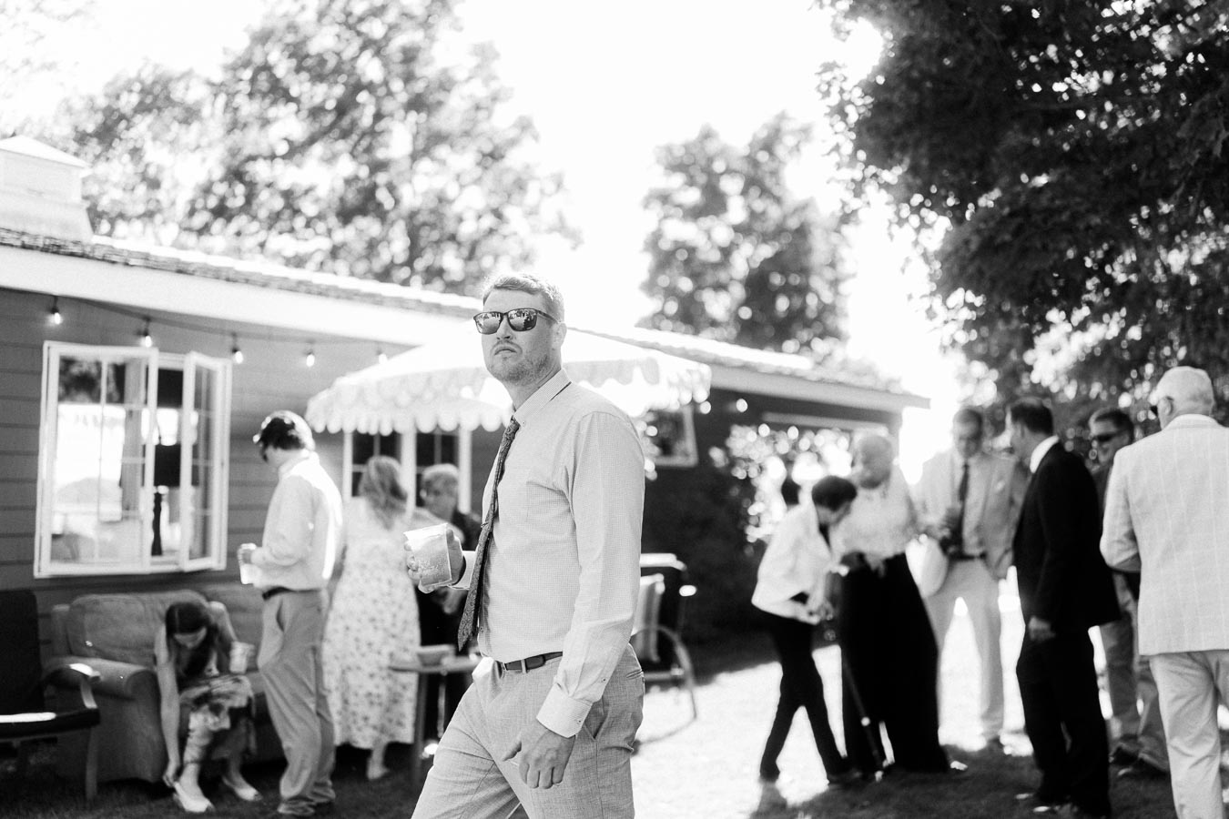 Black and white outdoor wedding reception on a private farm estate near Chatham-Kent, Ontario, with guests mingling beside a tent and house.