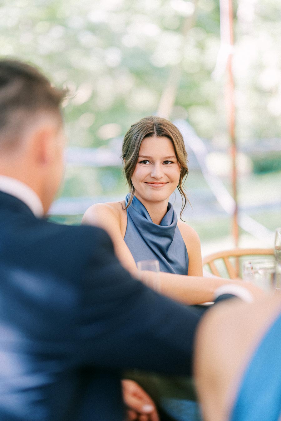Smiling woman at an outdoor tented wedding dinner on a private farm estate near Chatham-Kent, Ontario, with guests seated at a table.