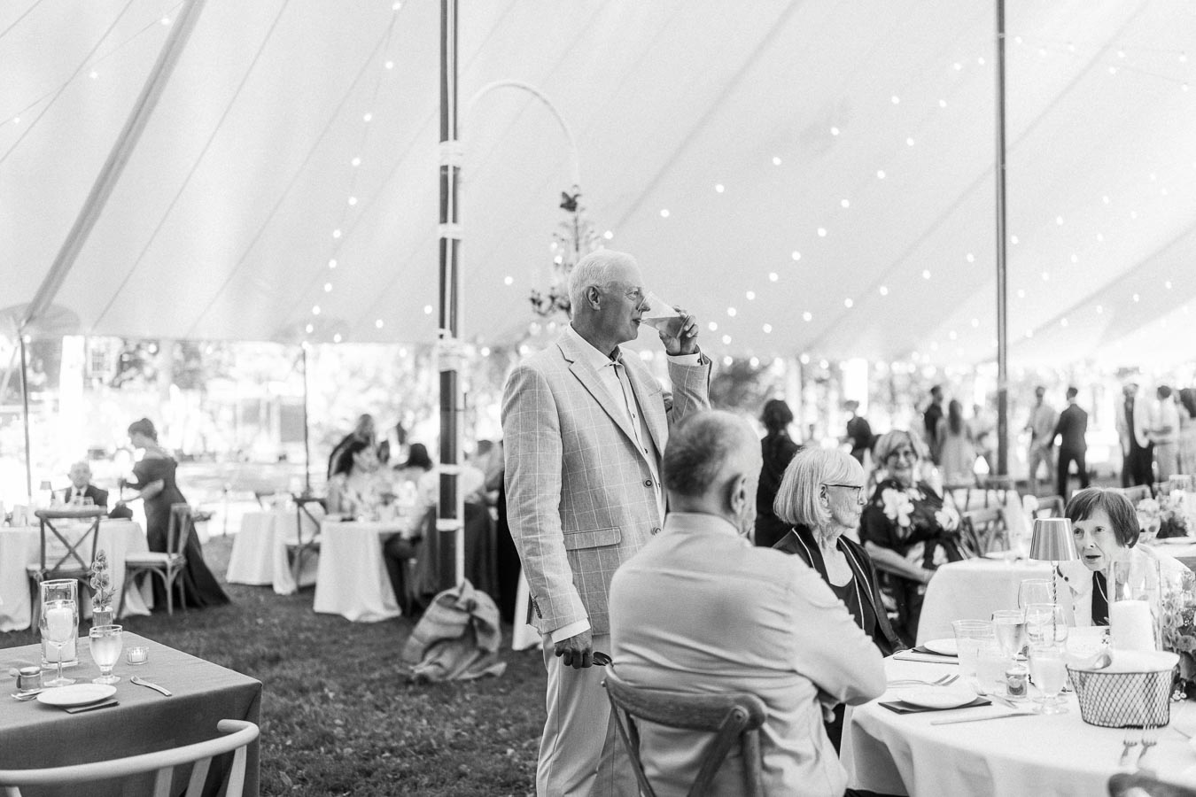 Black and white photo of guests seated at round tables inside a wedding tent on a private farm estate near Chatham-Kent, Ontario.
