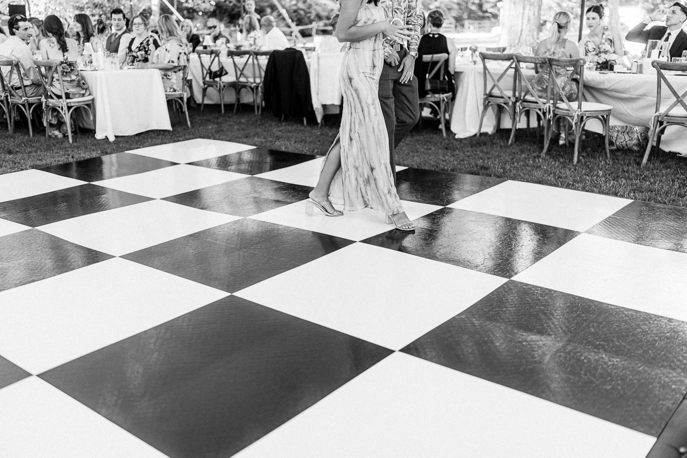 Black and white photo of guests dining under a tent while a couple dances on a checkered floor at an outdoor farm wedding in Chatham-Kent, Ontario.