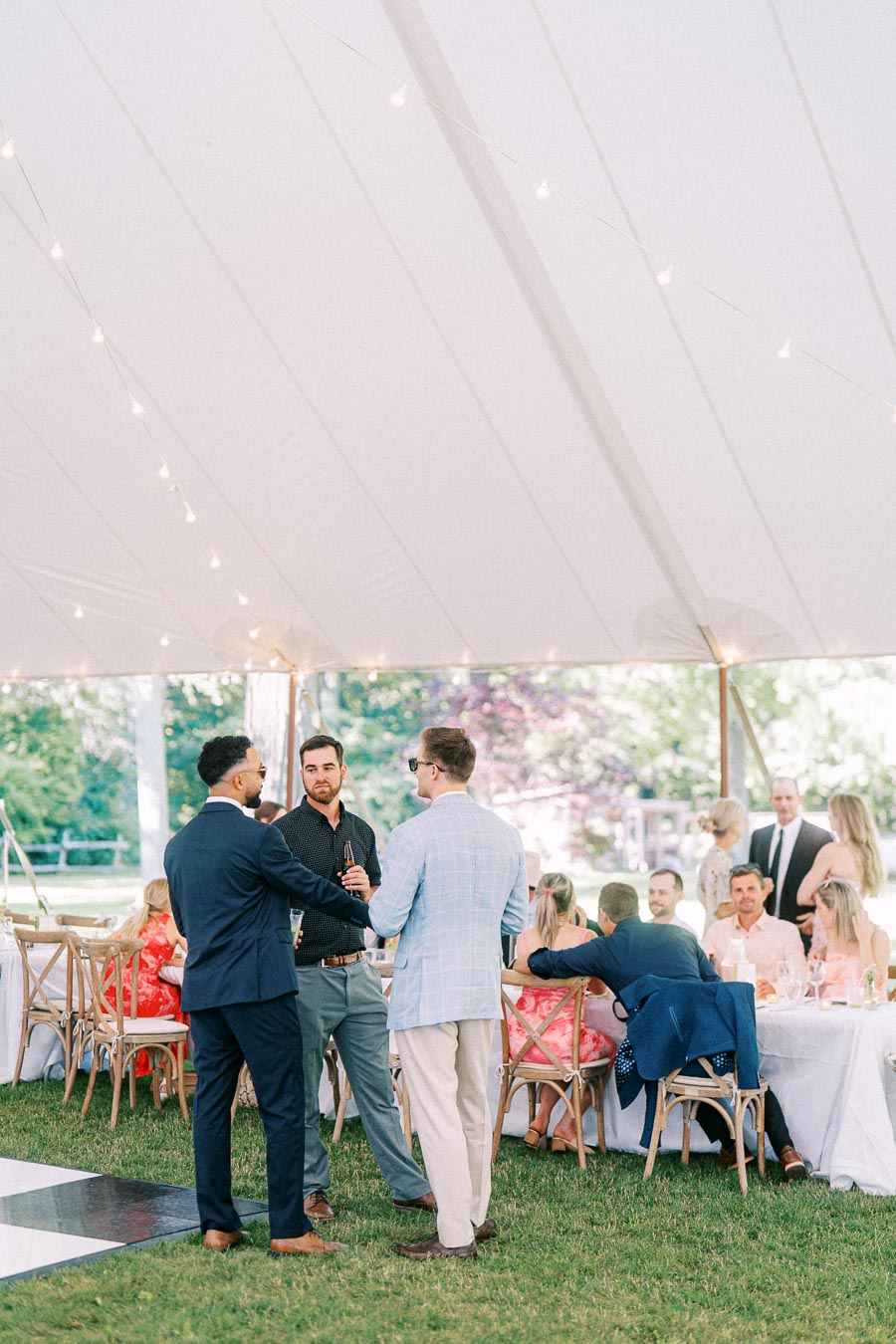 Wedding guests mingle under a white reception tent on a private farm estate near Chatham-Kent, Ontario, with string lights, tables, and chairs.