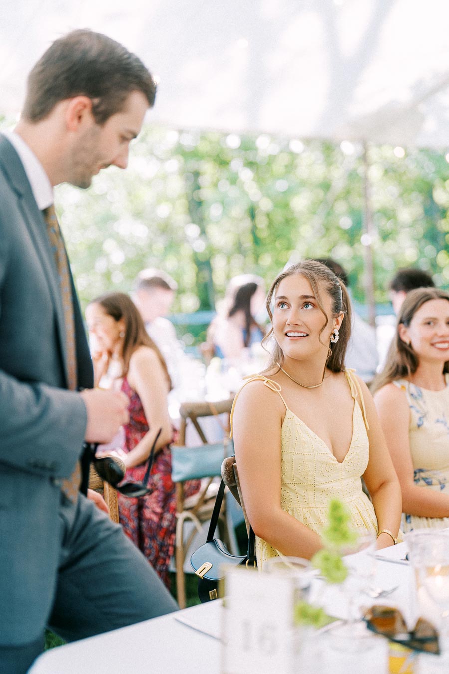 Guests talk and smile during a tented outdoor wedding dinner on a private farm estate near Chatham-Kent, Ontario, Canada.