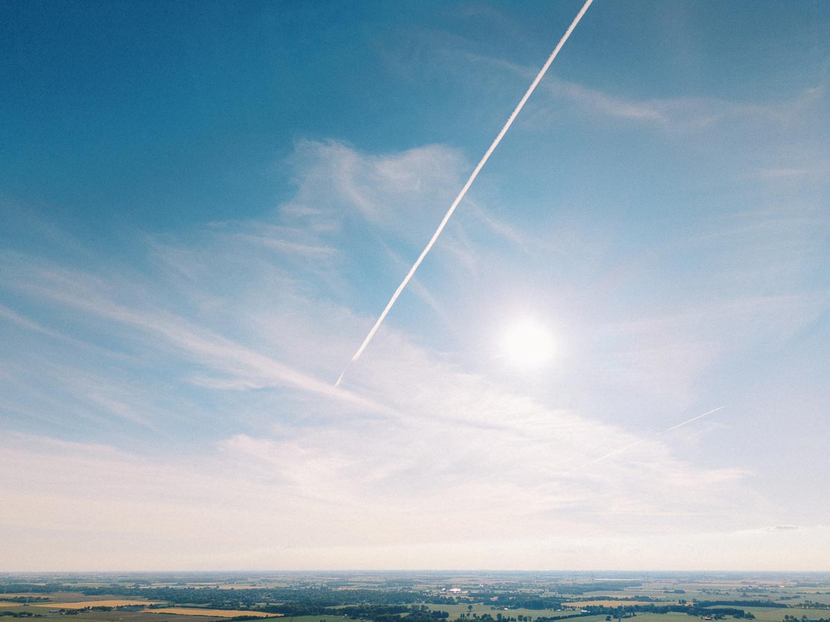 Bright blue sky with sun, contrail, and distant flat farmland near Chatham-Kent, Ontario, Canada.