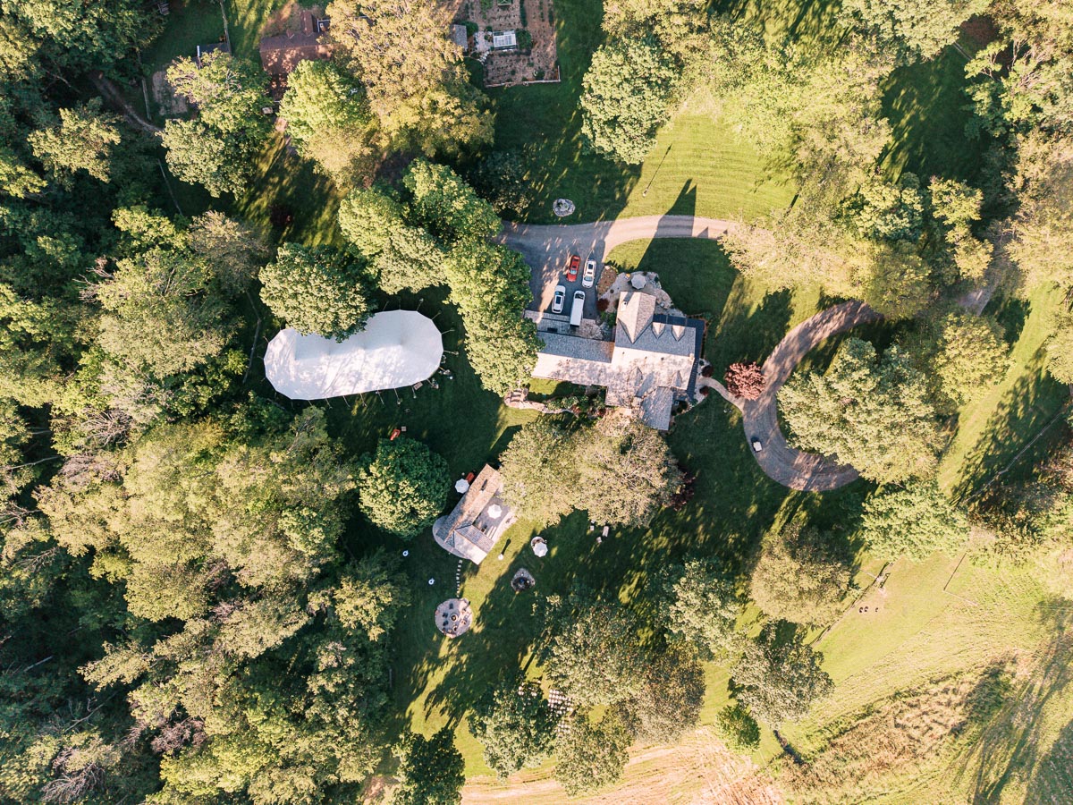 Aerial view of a private estate farm wedding setup with a white tent, house, driveway, cars, lawns, and trees near Chatham-Kent, Ontario, Canada.