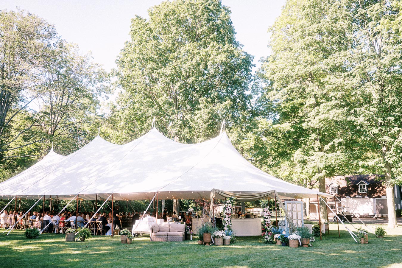 White wedding reception tent on a private farm estate near Chatham-Kent, Ontario, with guests dining outdoors among trees.