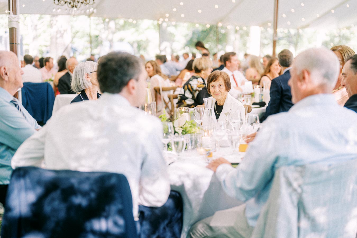 Wedding guests seated at round tables during a tented outdoor reception on a private estate near Chatham-Kent, Ontario, Canada.