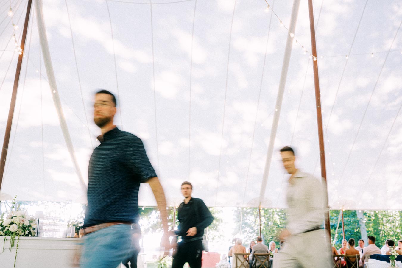 Blurred wedding guests walking under a large reception tent with string lights and seated guests at a private estate farm wedding near Chatham-Kent, Ontario.