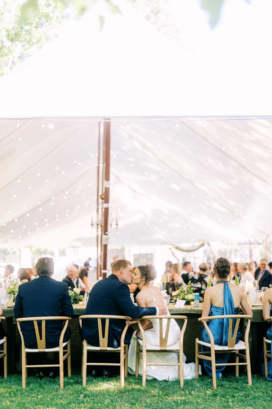 Bride and groom kiss at a long reception table during a tented outdoor wedding on a private estate near Chatham-Kent, Ontario, Canada.