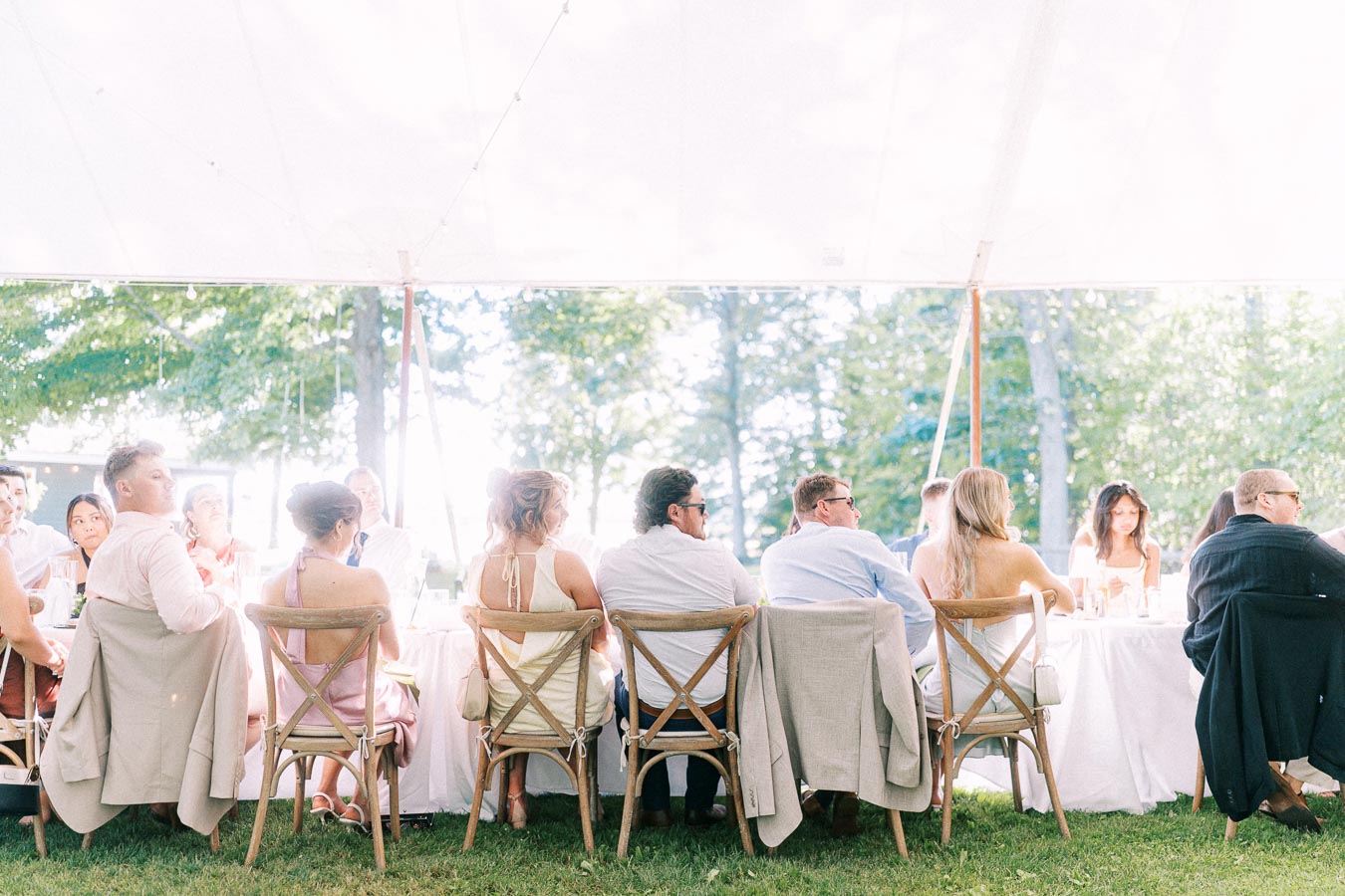 Wedding guests seated at round tables under a white reception tent on a grassy private farm property near Chatham-Kent, Ontario.
