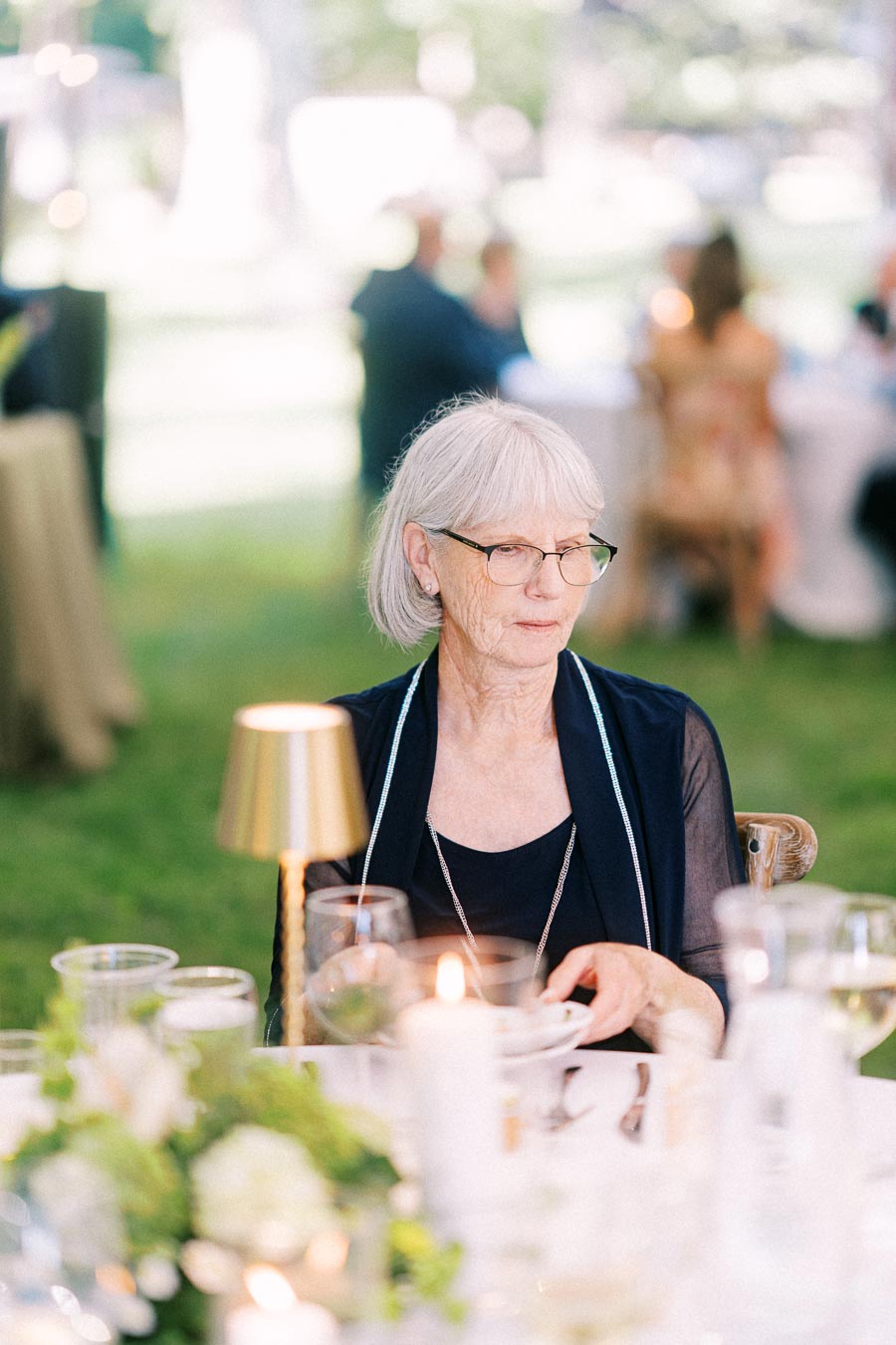 Elderly woman with glasses seated at a decorated table during an outdoor tented wedding dinner on a private estate near Chatham-Kent, Ontario.