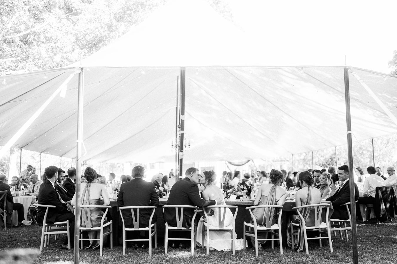 Black and white photo of wedding guests seated for an outdoor farm reception dinner under a large tent near Chatham-Kent, Ontario, Canada.