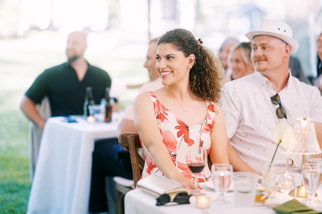 Smiling wedding guests seated at round tables under a tent during an outdoor farm wedding reception near Chatham-Kent, Ontario, Canada.