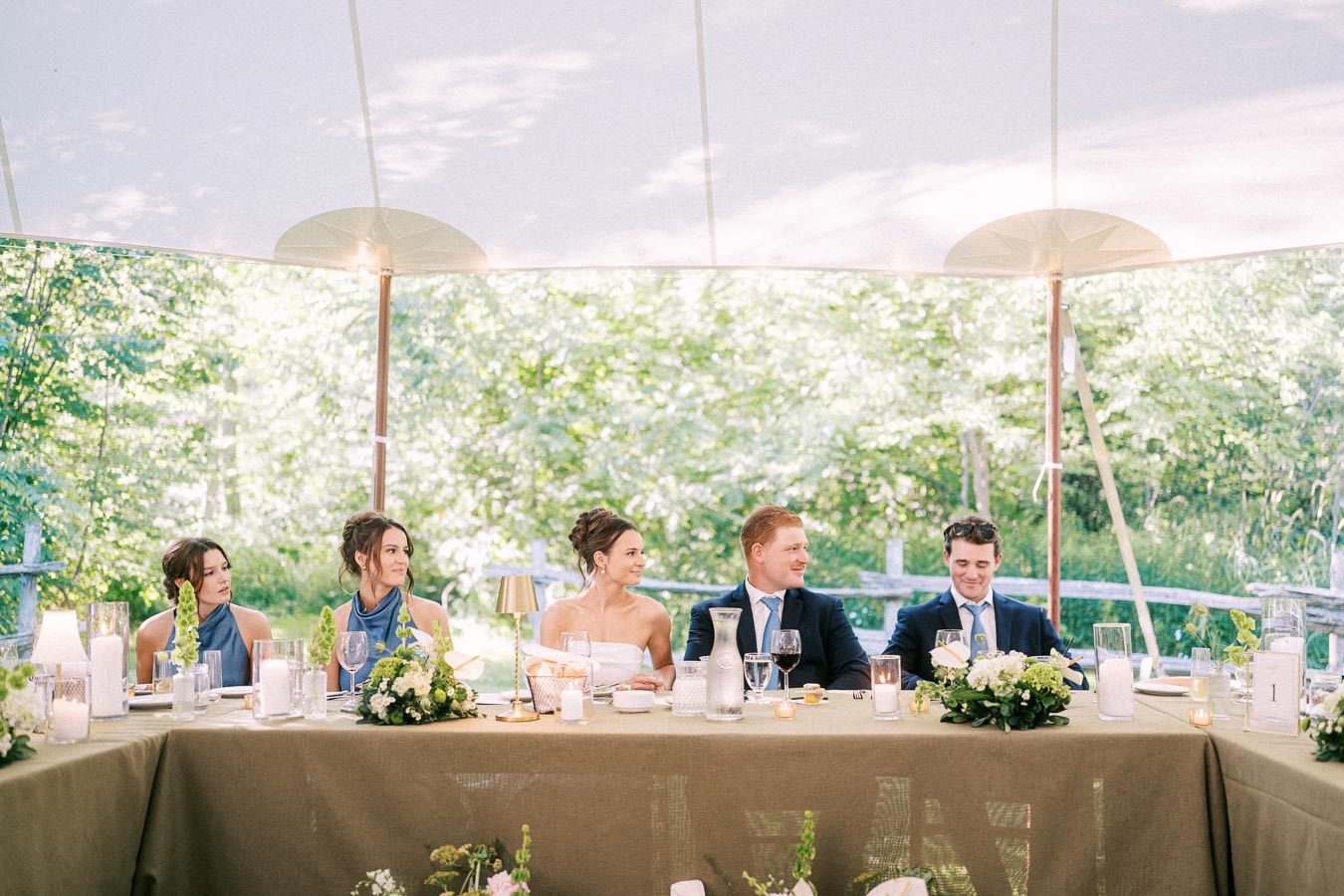 Bride, groom, and wedding party seated at a head table under a tent during an outdoor farm wedding near Chatham-Kent, Ontario.