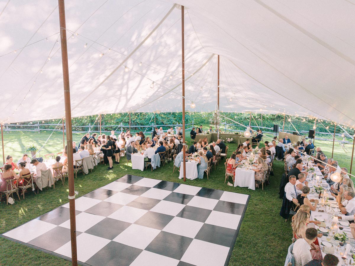Outdoor tented wedding reception on a private estate farm near Chatham-Kent, Ontario, with guests dining beside a checkered dance floor.