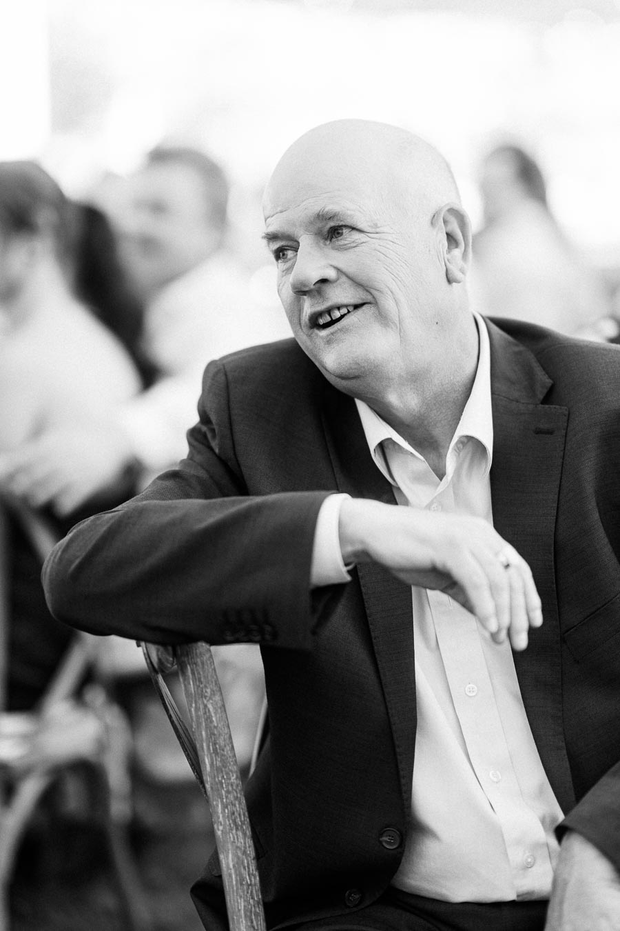 Black and white portrait of a smiling man in a suit seated at an outdoor wedding reception near Chatham-Kent, Ontario.