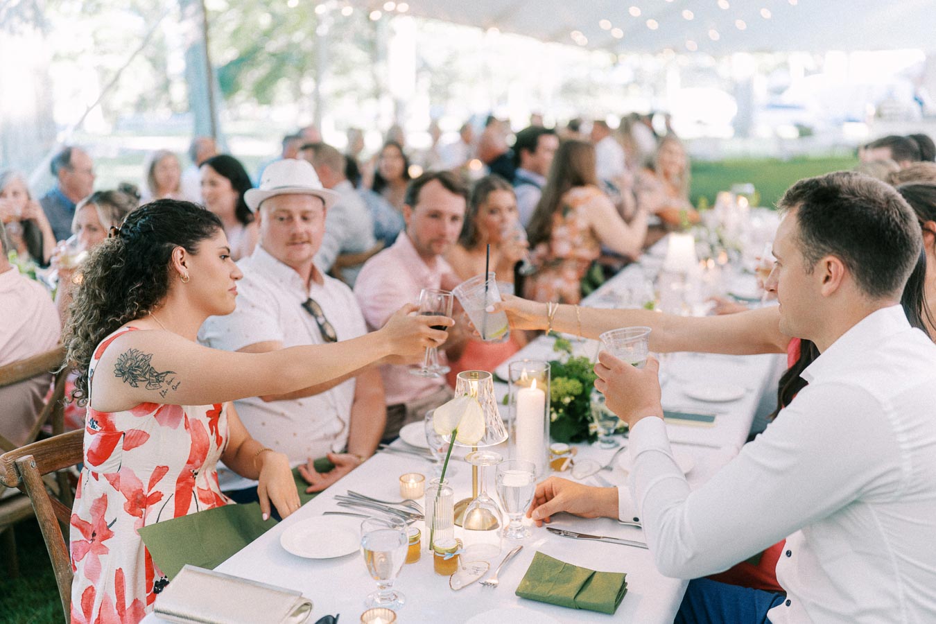 Wedding guests toast at a long dinner table under a tent on a private farm estate near Chatham-Kent, Ontario, Canada.