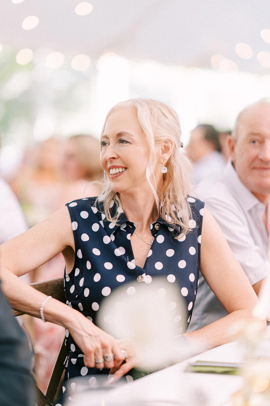 Smiling woman in a polka dot dress seated at a tented outdoor wedding reception near Chatham-Kent, Ontario, Canada.