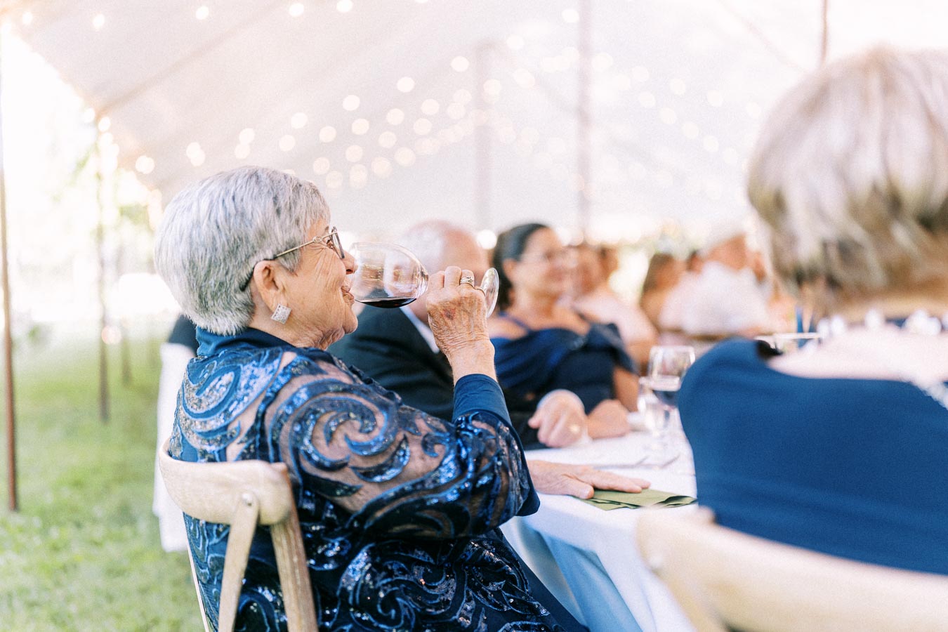 Older woman drinking red wine during an outdoor tented wedding dinner on a private farm estate near Chatham-Kent, Ontario, Canada.