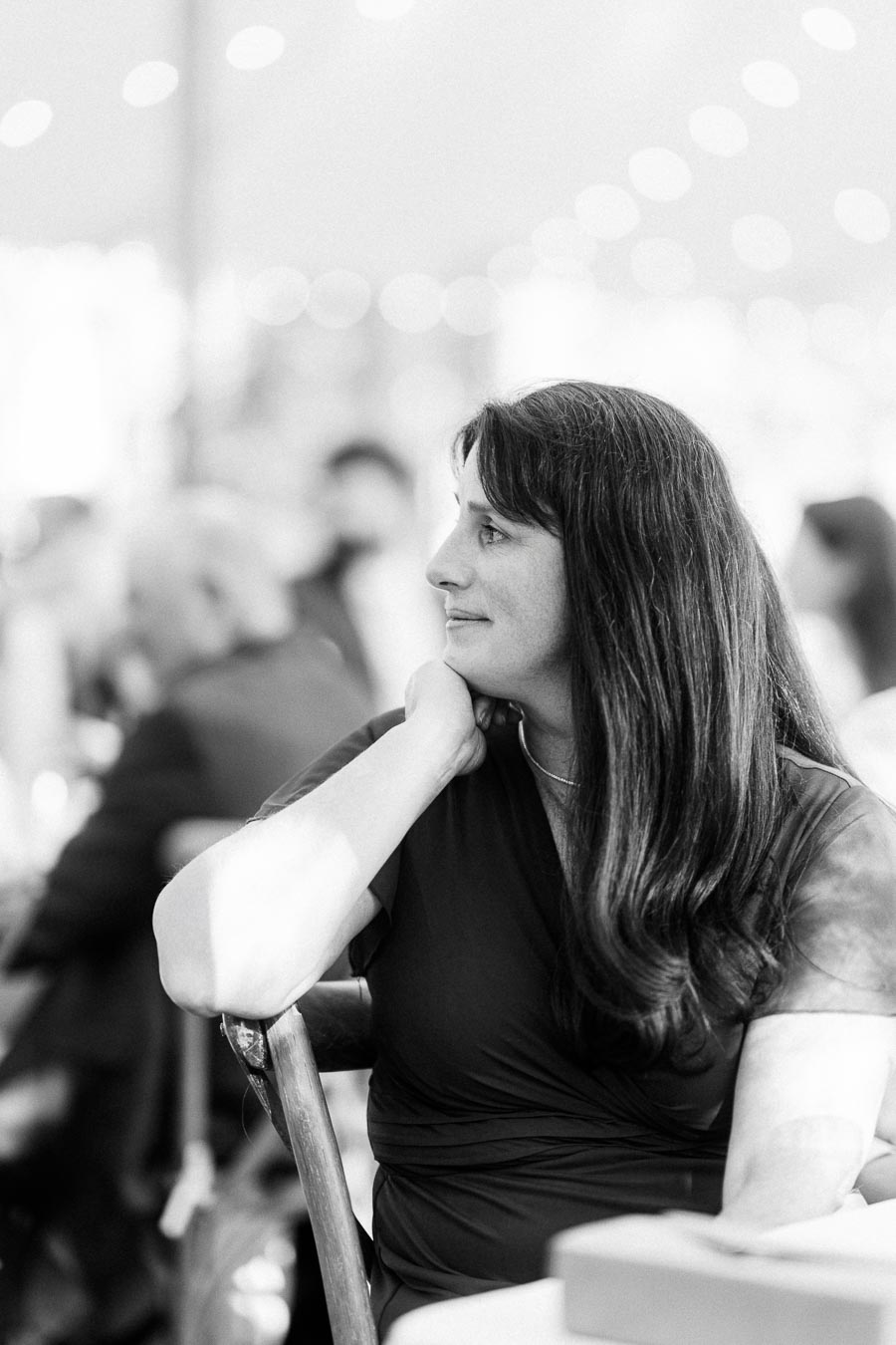 Black and white portrait of a seated woman at a tented wedding reception near Chatham-Kent, Ontario, with blurred guests and string lights.