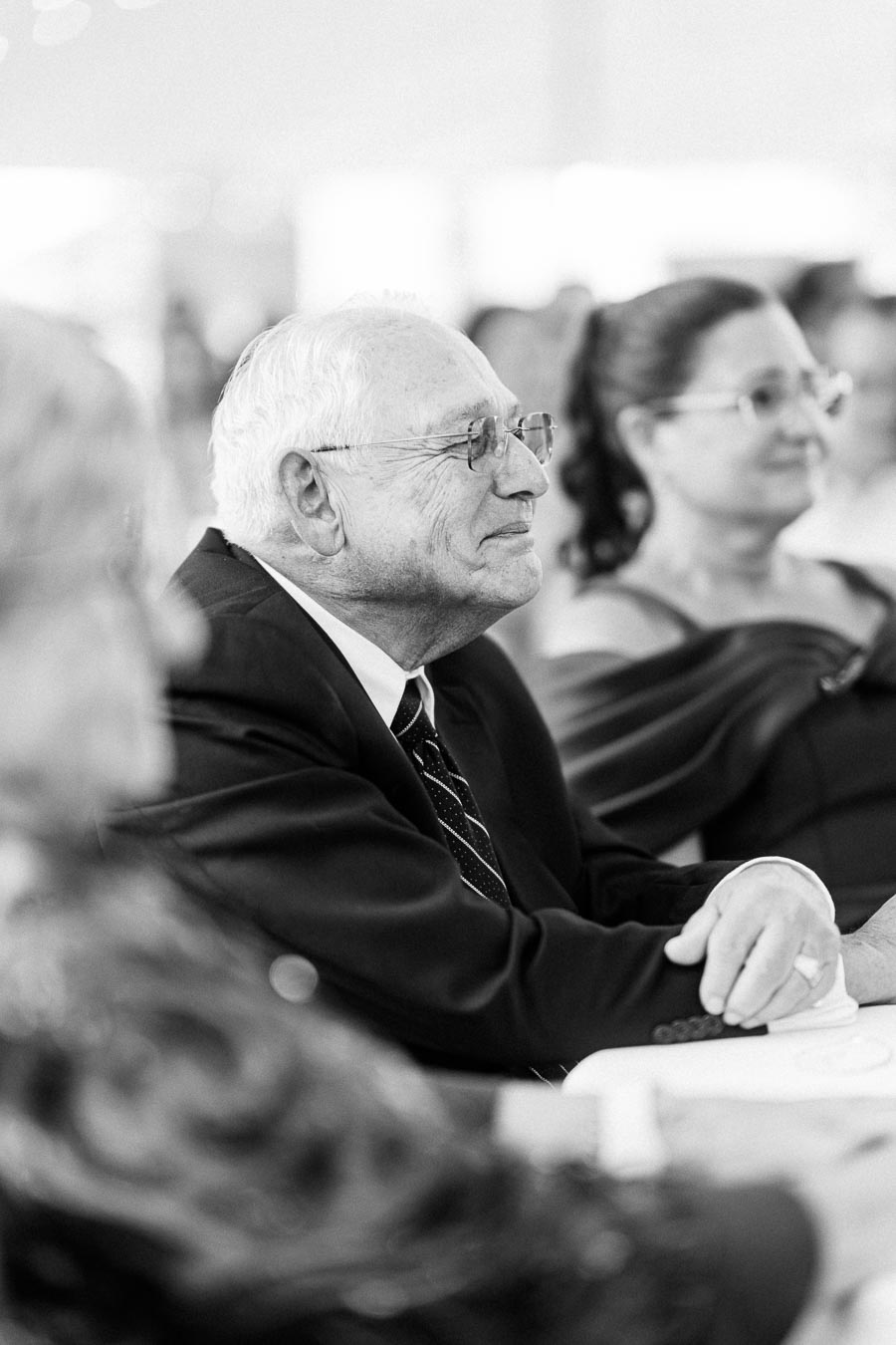 Black and white photo of an elderly man in a suit and glasses seated at a wedding reception table inside a tent near Chatham-Kent, Ontario.