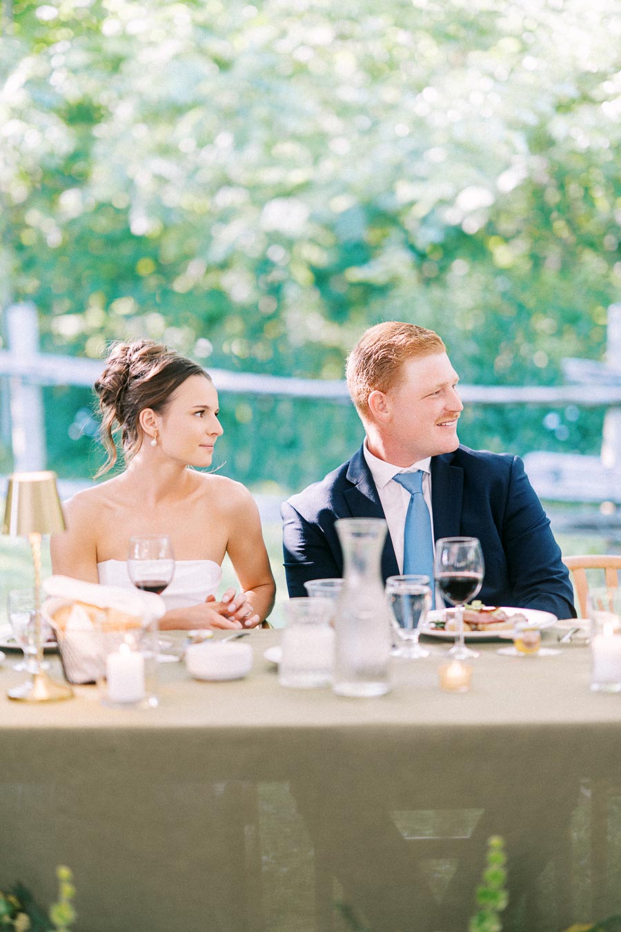 Bride and groom seated at an outdoor wedding dinner table on a private estate near Chatham-Kent, Ontario, with wine glasses, candles, and greenery.