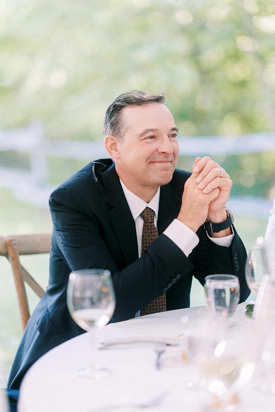 Smiling man in a dark suit seated at an outdoor wedding reception table near Chatham-Kent, Ontario, Canada.
