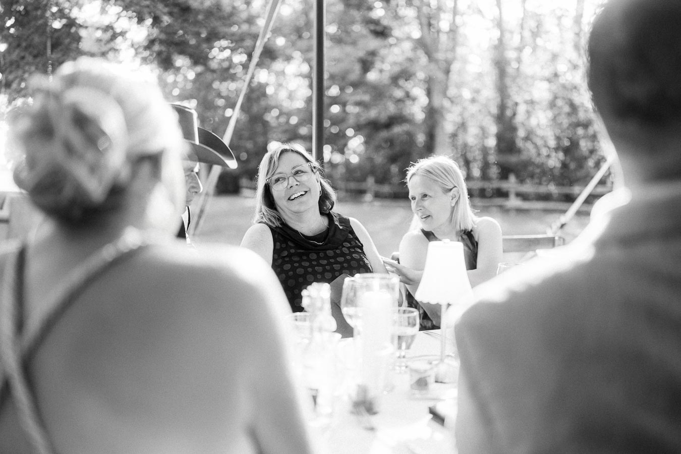 Black and white photo of wedding guests laughing during an outdoor tented dinner on a private farm estate near Chatham-Kent, Ontario, Canada.