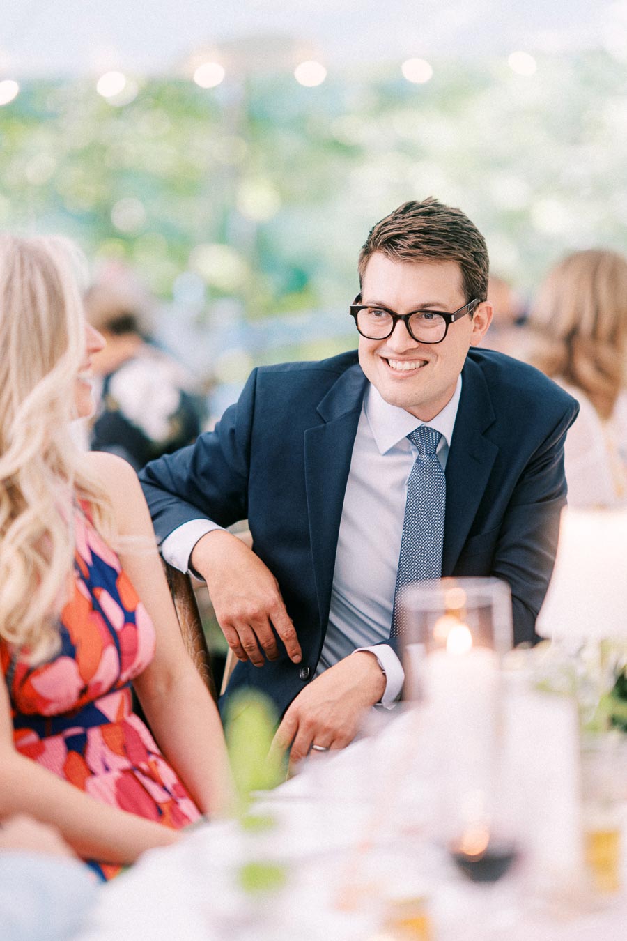 Smiling male guest in a navy suit talking with a woman during a tented outdoor wedding reception near Chatham-Kent, Ontario.