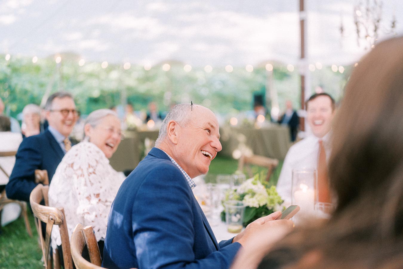 Smiling wedding guests seated at a dinner table under a tent on a private farm estate near Chatham-Kent, Ontario, Canada.