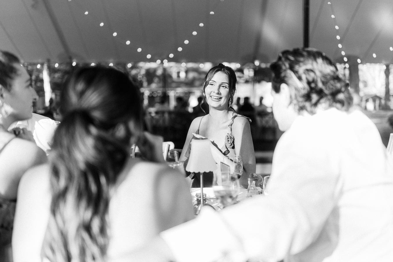 Black and white photo of wedding guests talking and smiling during a tented dinner on a private estate near Chatham-Kent, Ontario, Canada.