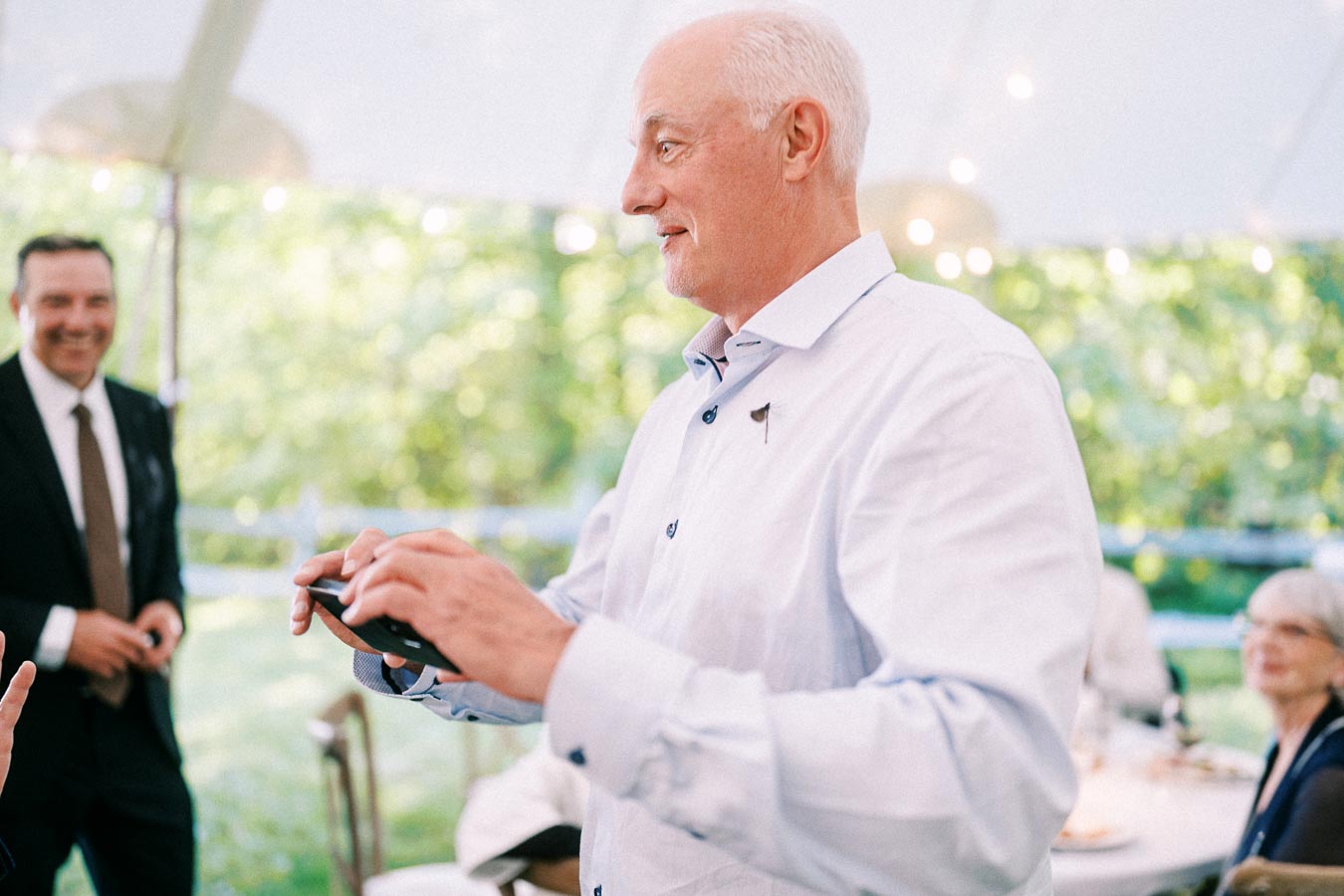Older man giving a speech under a white tent at an outdoor private estate wedding reception near Chatham-Kent, Ontario, Canada.