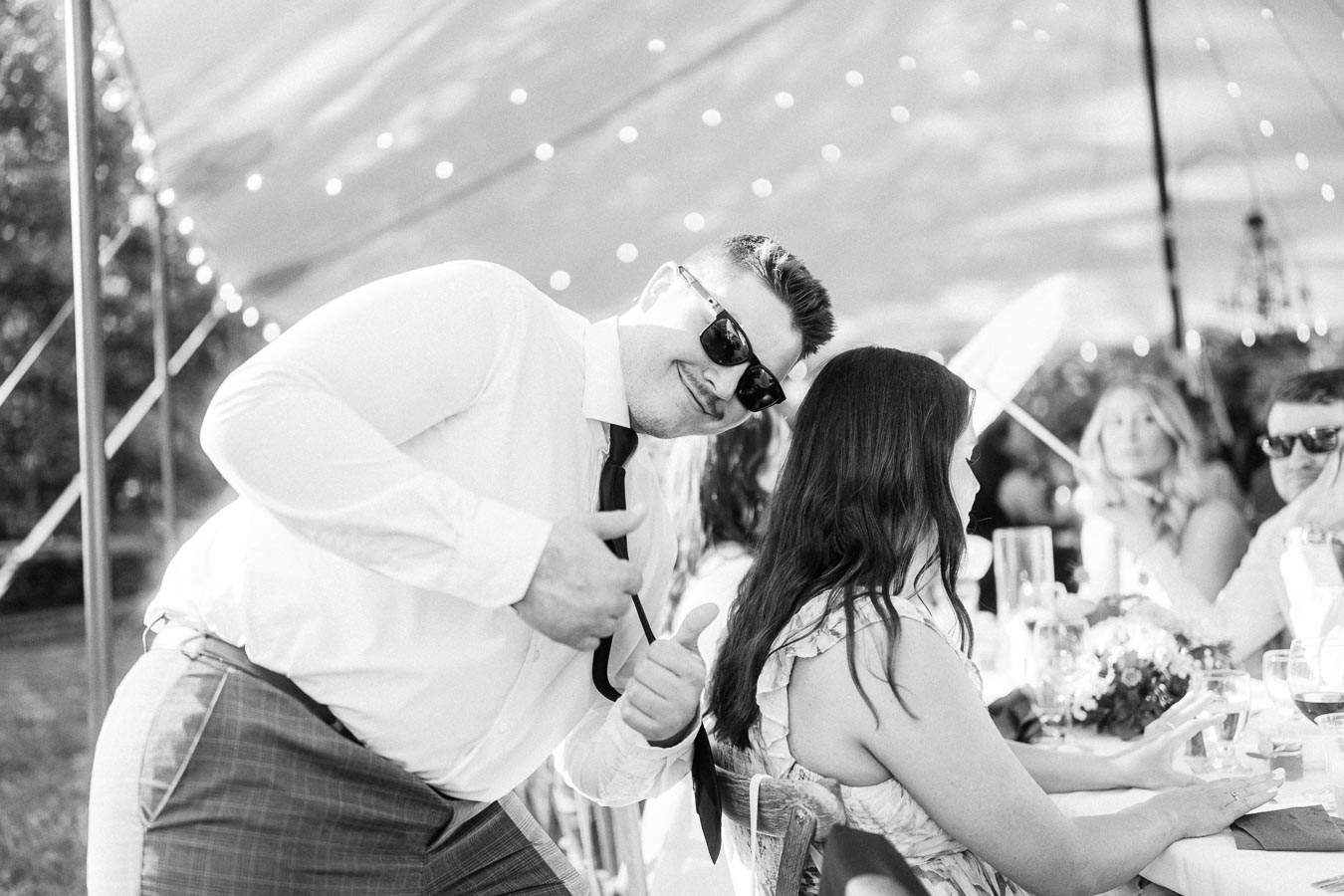 Black and white photo of wedding guests dining under a tent on a private farm estate near Chatham-Kent, Ontario, with a man in sunglasses posing.