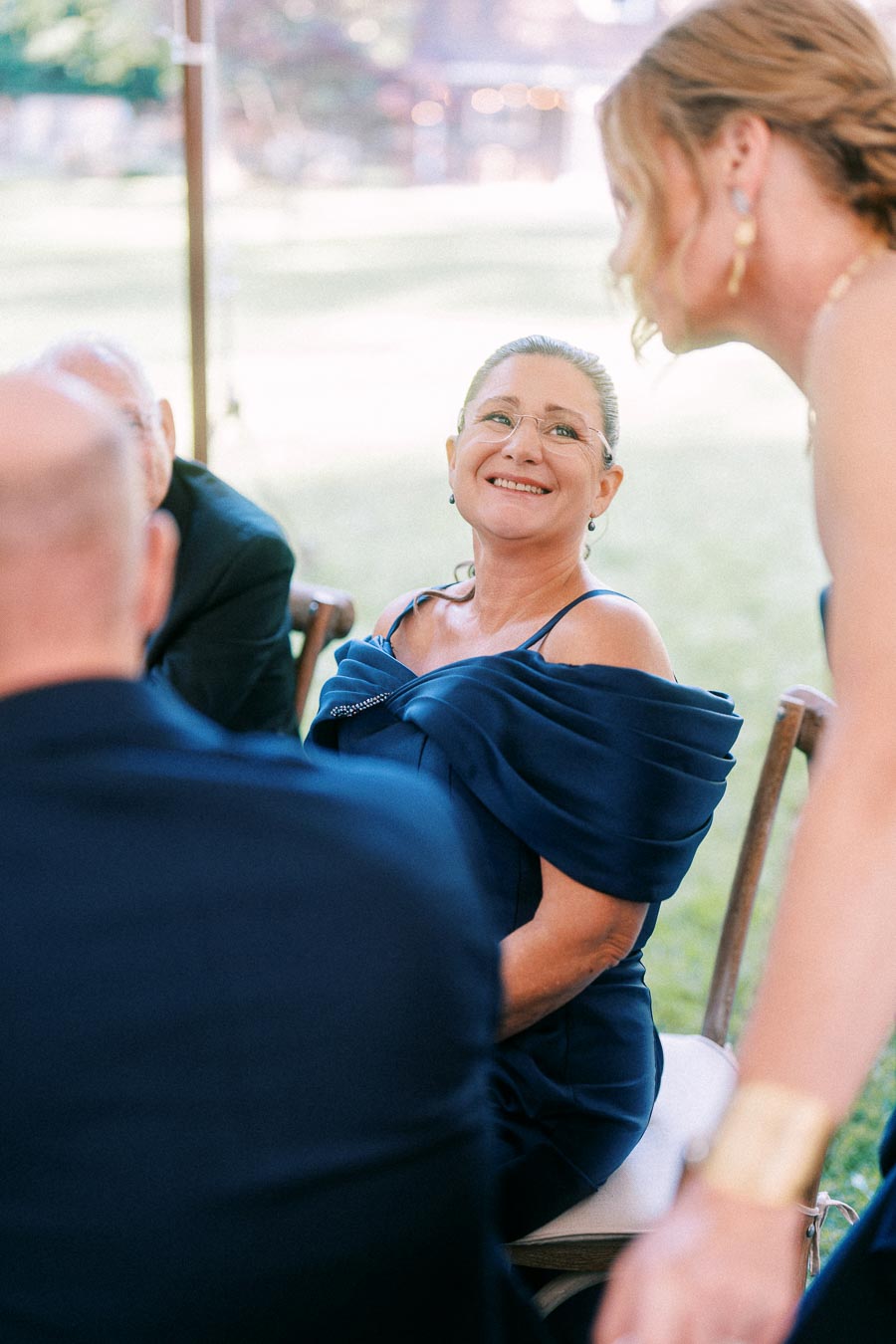 Smiling woman in a navy dress seated with wedding guests during an outdoor tented farm reception near Chatham-Kent, Ontario.