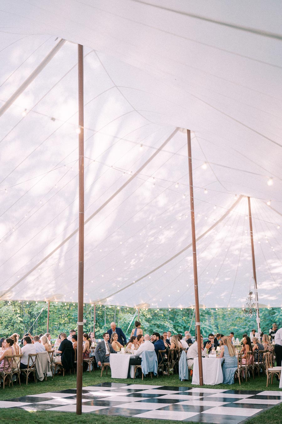 Wedding guests dining under a white tent with string lights and a black and white dance floor on a private farm estate near Chatham-Kent, Ontario, Canada.