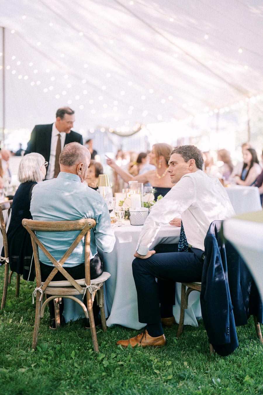 Wedding guests seated at round dinner tables under a white reception tent on grass near Chatham-Kent, Ontario, Canada.