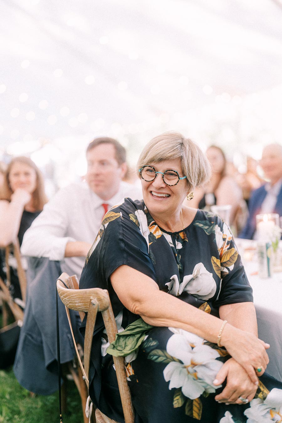 Smiling woman seated among wedding guests during a tented outdoor reception on a private farm estate near Chatham-Kent, Ontario, Canada.