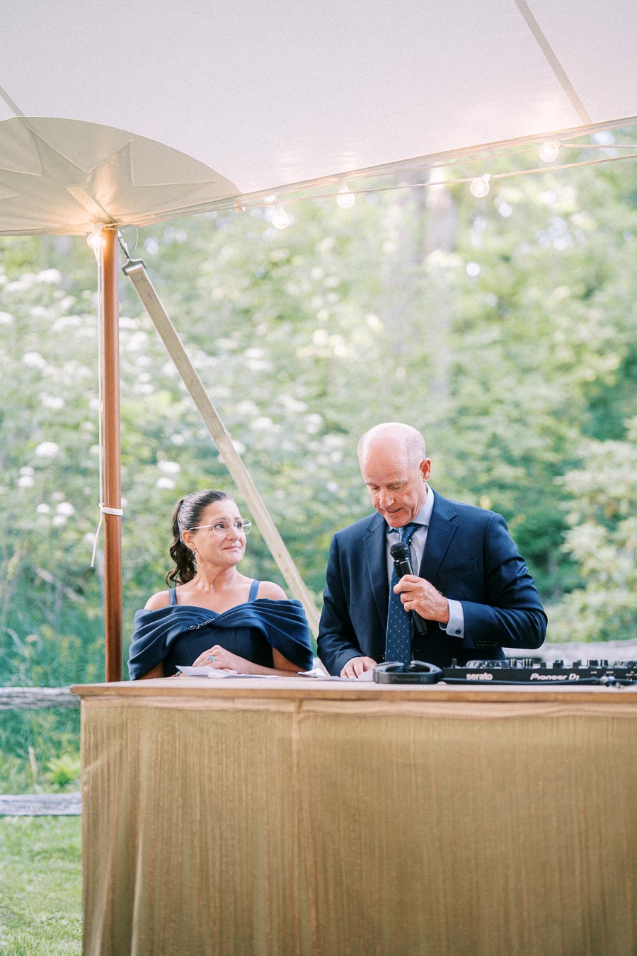 Man and woman at a wooden DJ booth during an outdoor tented wedding reception on a private farm estate near Chatham-Kent, Ontario.