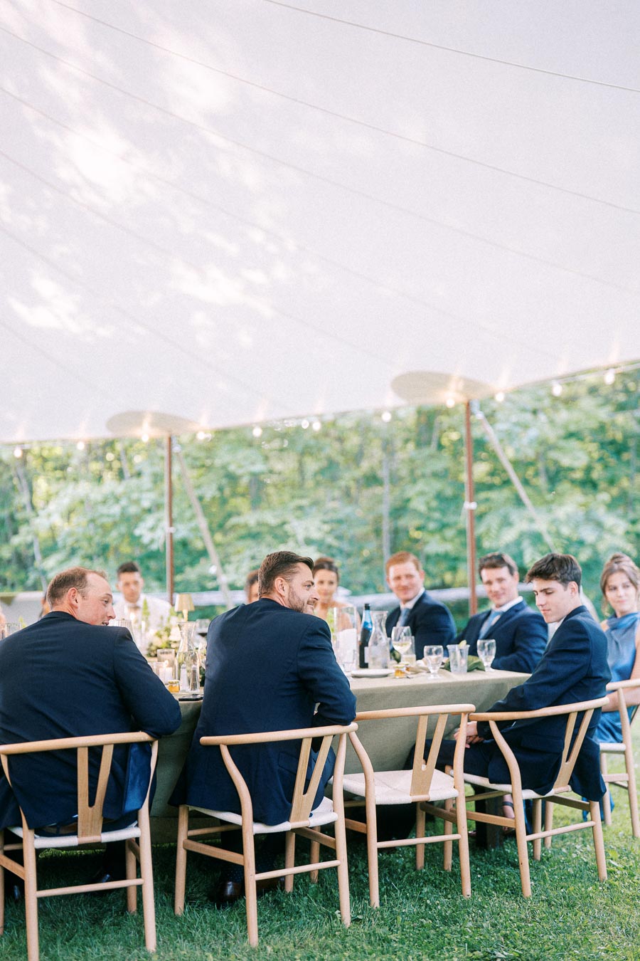Wedding guests seated at a long outdoor dinner table under a white tent on a grassy private farm property near Chatham-Kent, Ontario.