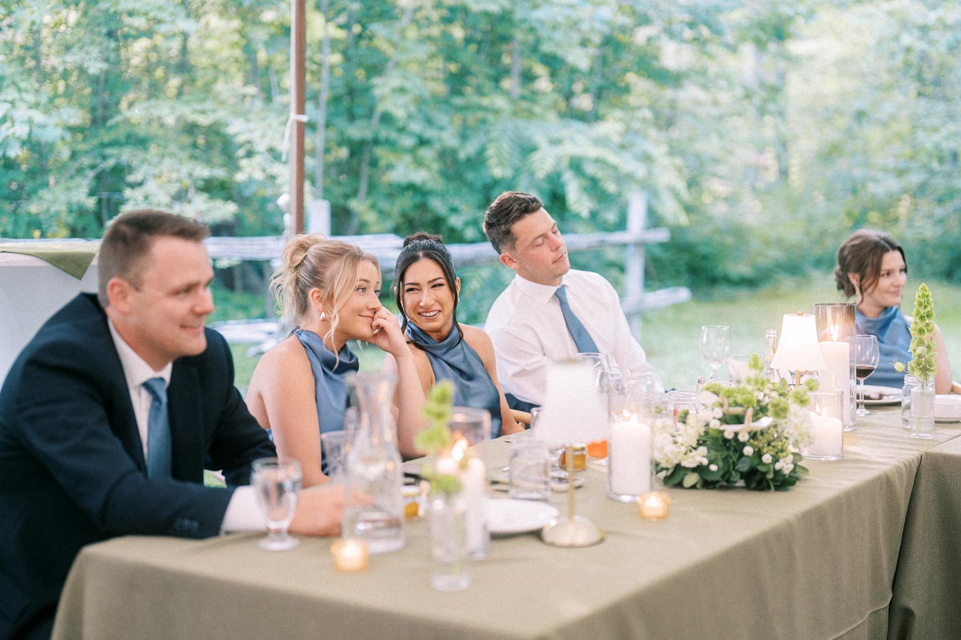 Wedding guests seated at an outdoor tented farm reception table with candles, flowers, glassware, and greenery near Chatham-Kent, Ontario.
