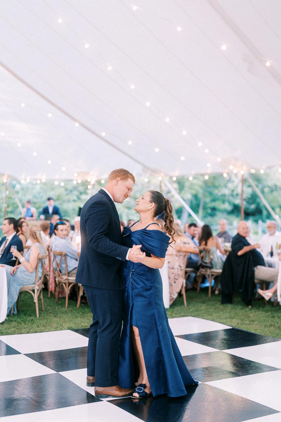 Couple slow dancing on a black and white checkered dance floor under a white tent during an outdoor private estate wedding near Chatham-Kent, Ontario, Canada.