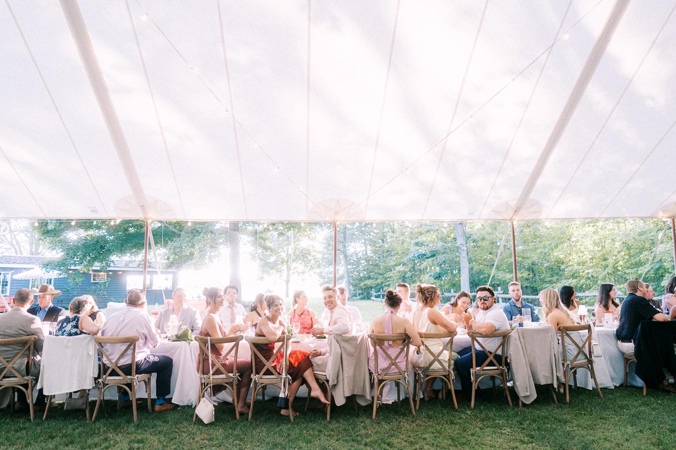 Wedding guests seated at long tables under a white outdoor reception tent on a private farm property near Chatham-Kent, Ontario, Canada.
