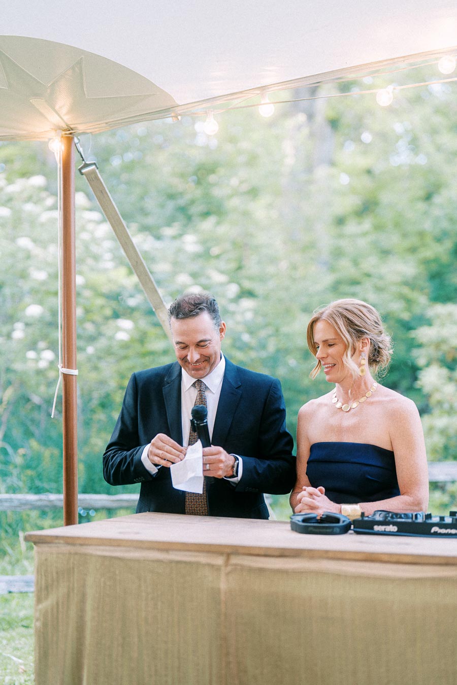 Man speaking into a microphone beside a woman at an outdoor tented wedding reception on a private farm estate near Chatham-Kent, Ontario.