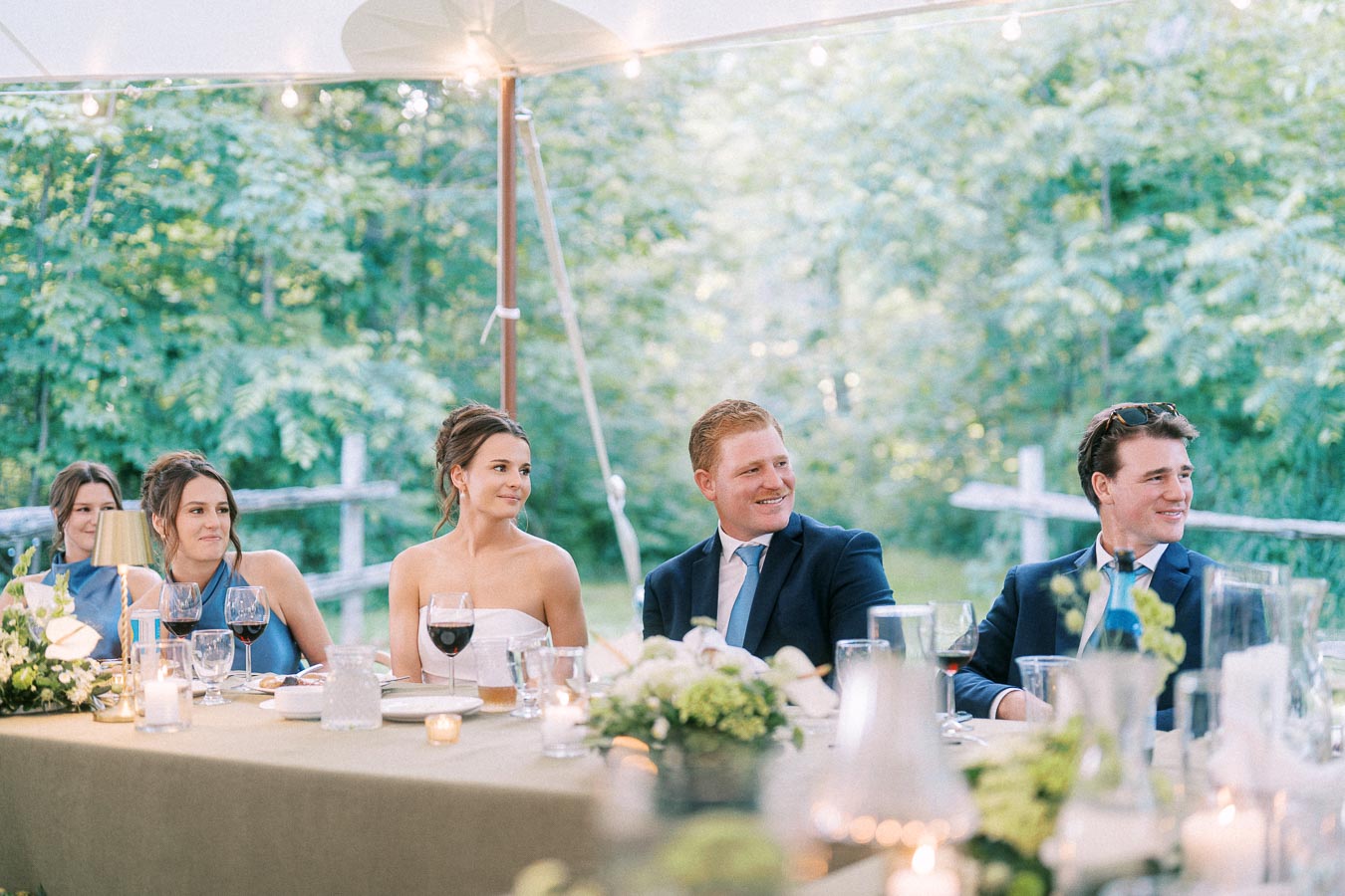 Bride, groom and guests seated at a tented outdoor wedding dinner on a private farm estate near Chatham-Kent, Ontario, with candles, wine and flowers.
